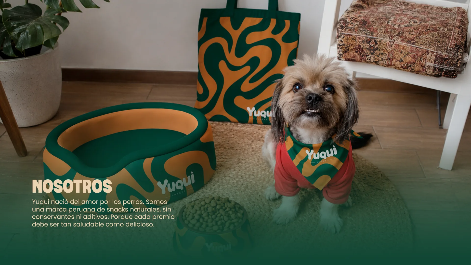 Nosotros: Yuqui nació del amor por los perros. Somos una marca peruana de snacks naturales, sin conservantes ni aditivos. Porque cada premio debe ser tan saludable como delicioso. Un perrito con pañuelo Yuqui junto a una cama y un plato de la marca.